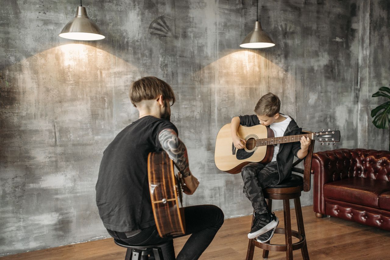 A boy learning acoustic guitar from a teacher in a modern studio setting.